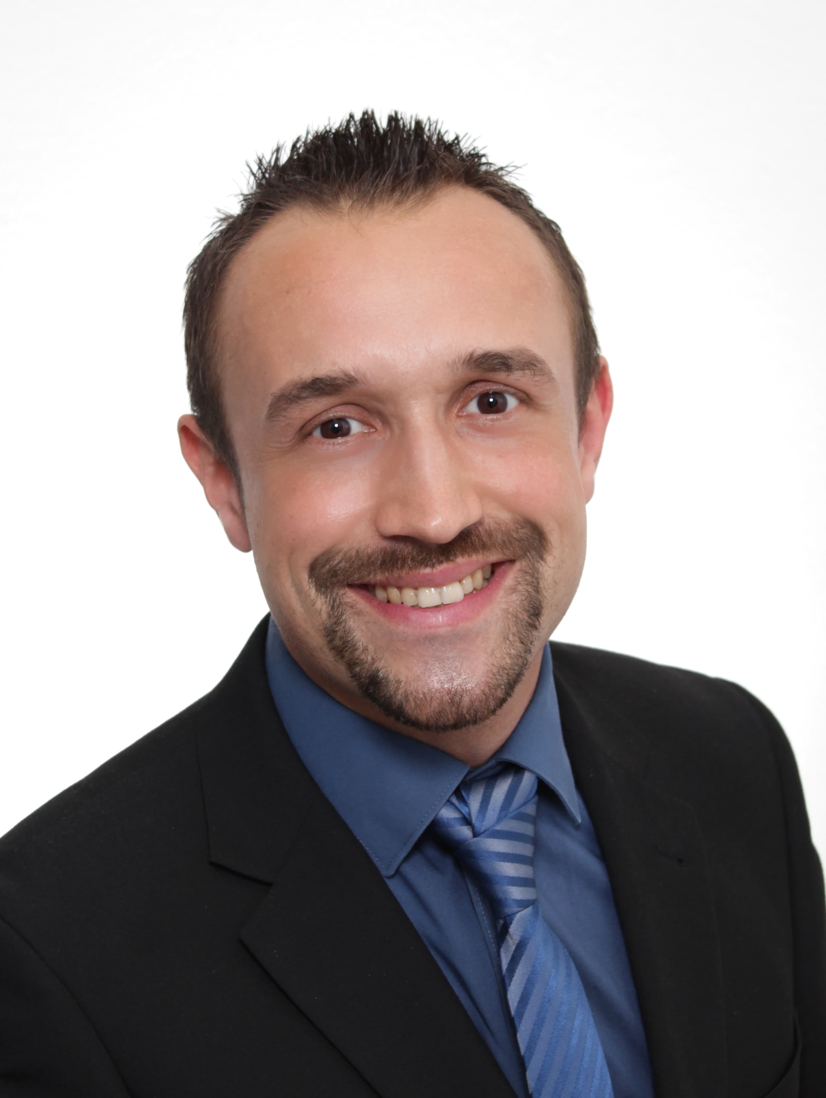 Smiling man in black suit, blue shirt, and striped tie with a goatee.