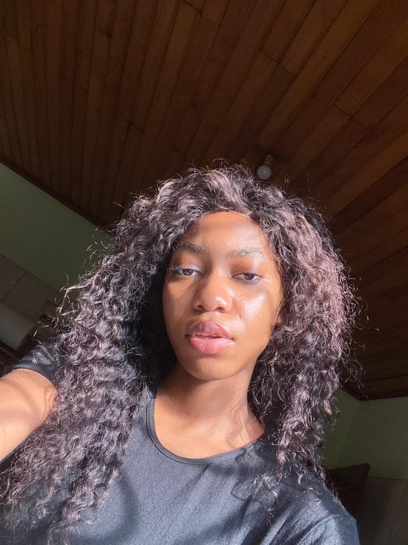 Young Black woman with voluminous curly hair looks at the camera in bright sunlight.